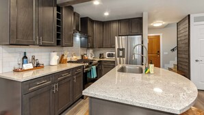 A modern kitchen with dark wood cabinets, a granite countertop, stainless steel appliances, and a built-in oven. - Stylish Sun Valley 2BR - Dog-Friendly - 2 Min Walk to Town (Ketchum)