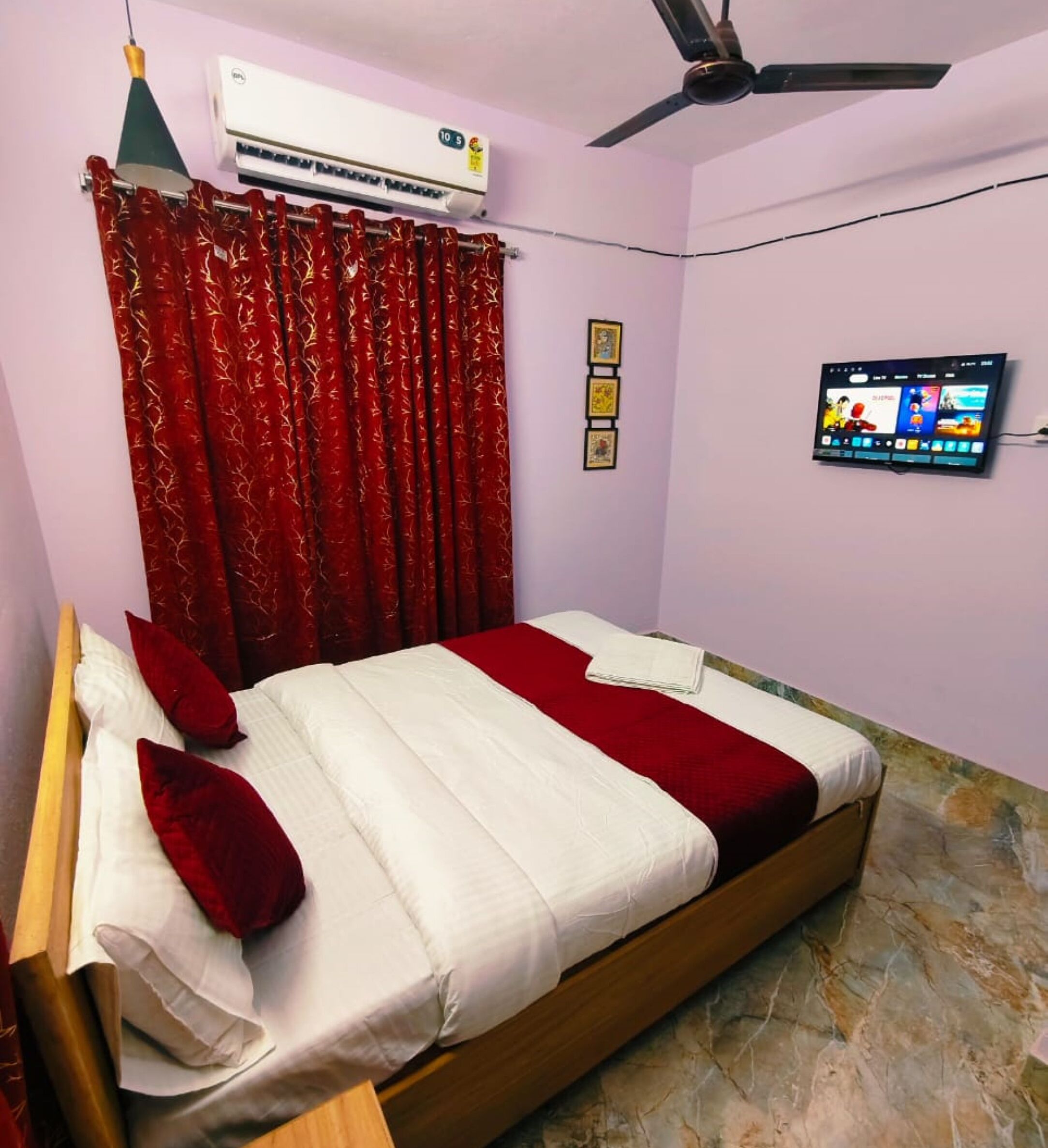 A bedroom with a bed, red curtains, an air conditioner, a ceiling fan, a TV, and a marble floor.