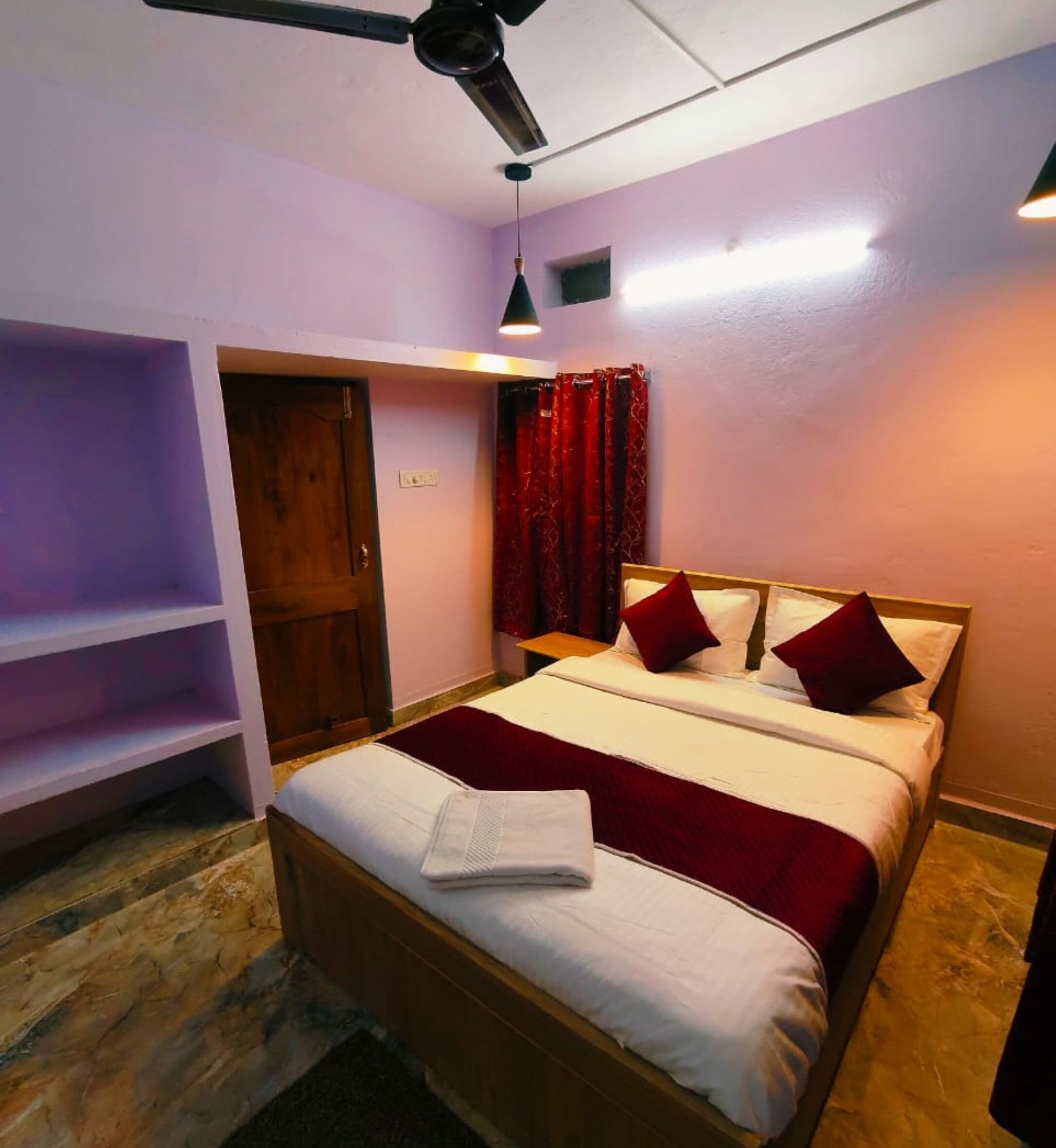 A bedroom with a bed, a ceiling fan, a red curtain, and a wooden door.
