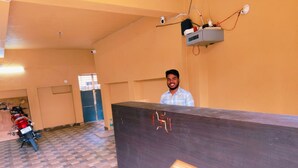 A reception desk with a person standing behind it, a motorcycle parked to the left, and a security camera on the ceiling. - Goroomgo Rail View Guest House Puri (Puri)