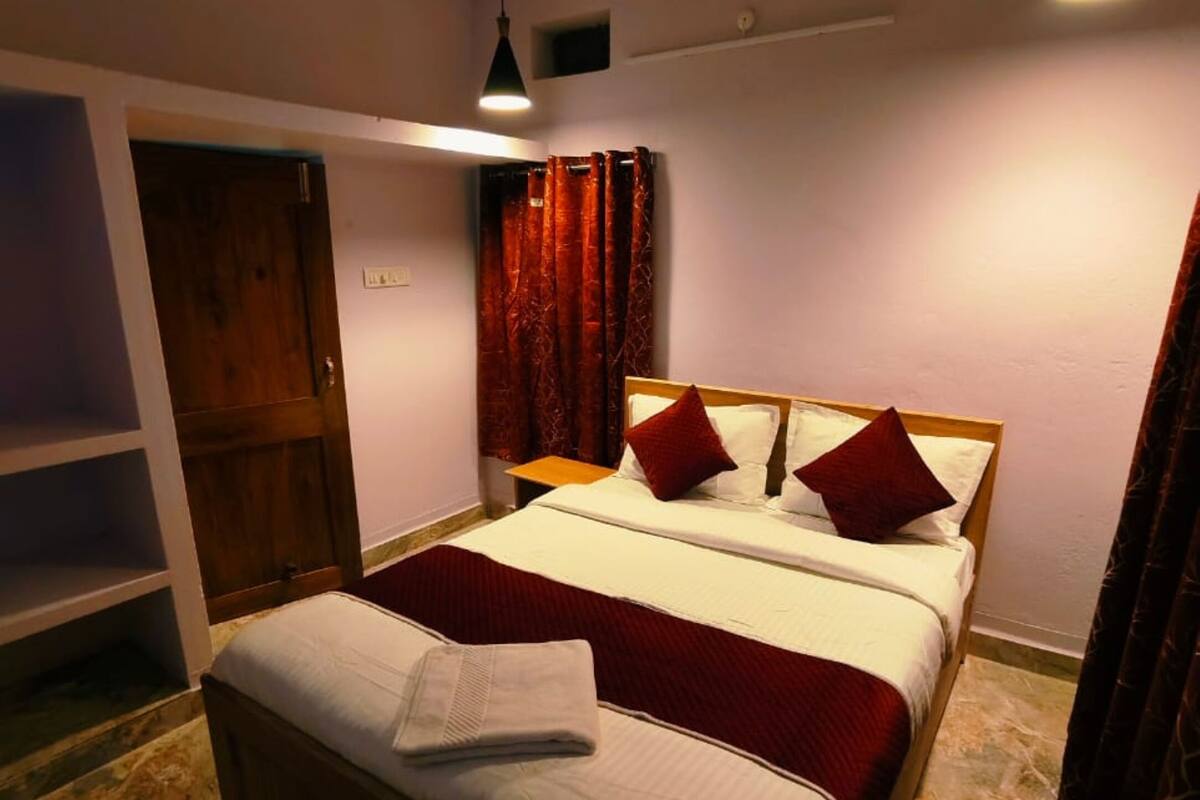 A bedroom with a bed, a wooden wardrobe, a small table, and a ceiling fan.