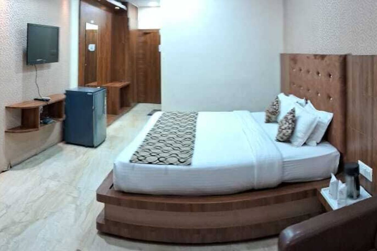 Habitación de hotel con cama, escritorio, televisión y un refrigerador pequeño.