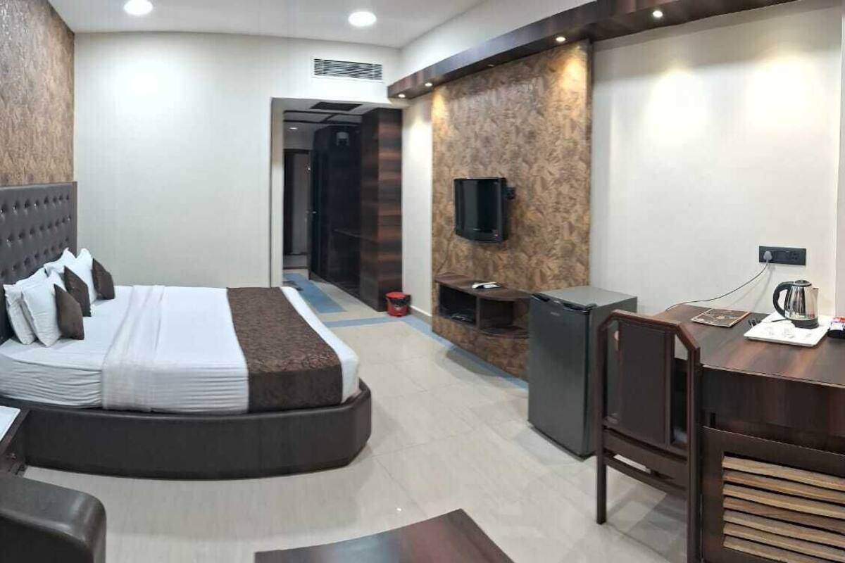 Una habitación de hotel con cama, escritorio, silla, televisor y un pequeño rincón de cocina.