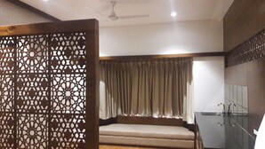 A hotel room with a bed, curtains, a ceiling fan, and a bathroom with a sink and mirror.