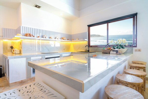 Una cocina moderna con una isla grande, vistas al océano y taburetes de madera.