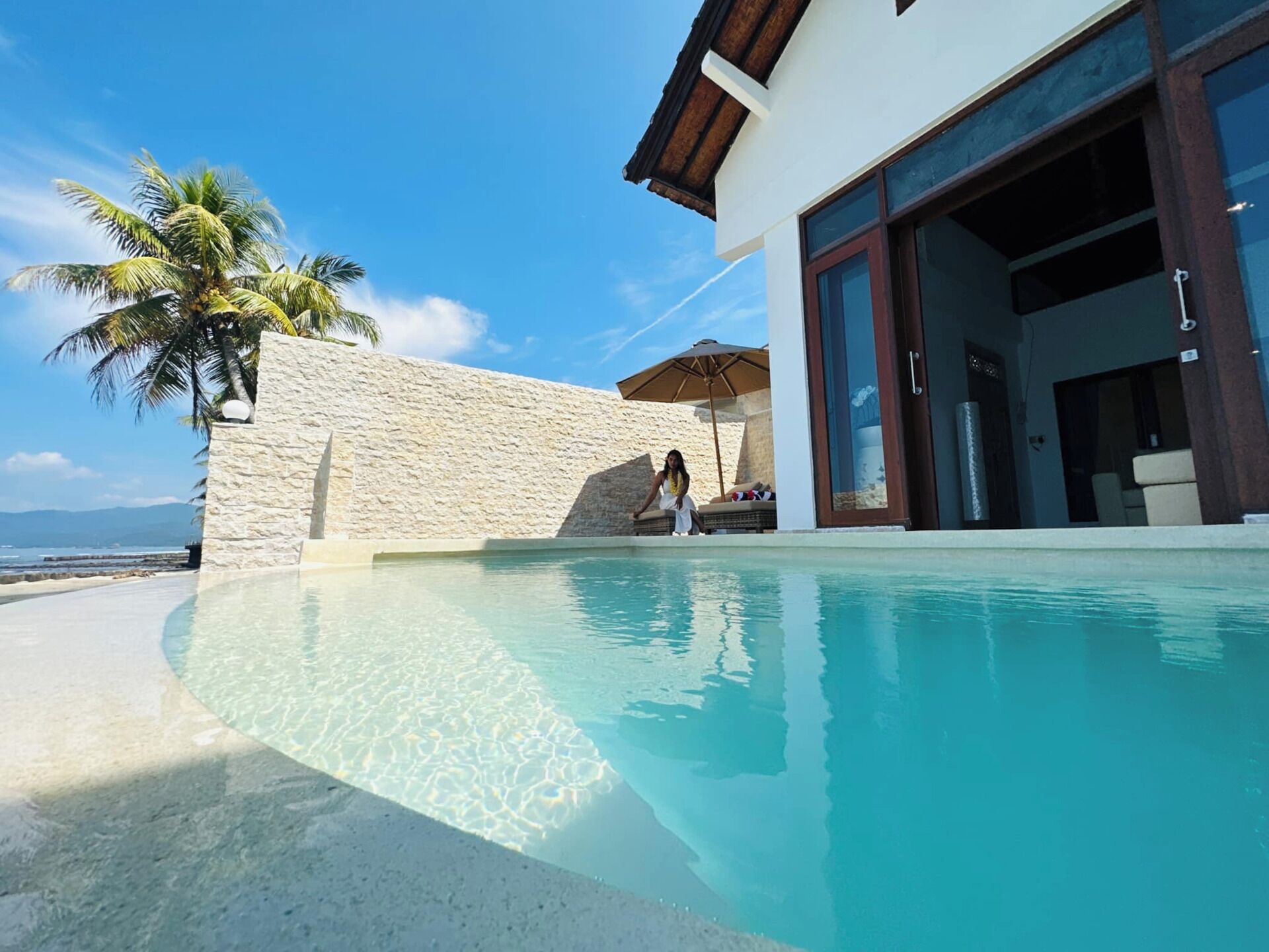 Uma área moderna na piscina, com piscina límpida, parede de pedra e uma palmeira.