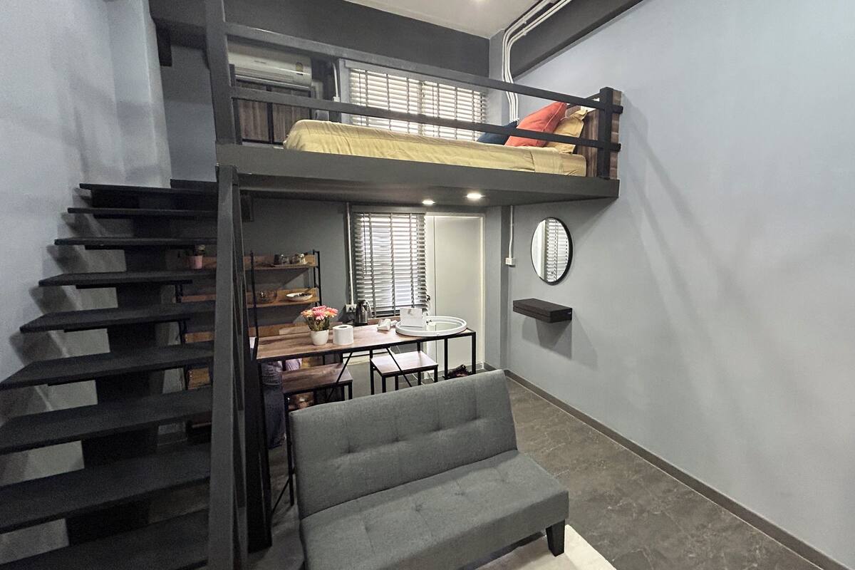 A compact room with a bunk bed, a dining table with chairs, and a gray sofa.