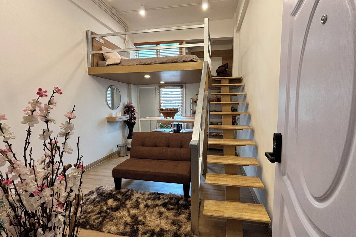 A compact room with a bunk bed, a small sofa, a fluffy rug, and a staircase.