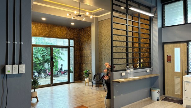 A modern reception area with a wooden reception desk, a large window with a view of the outside, and a ceiling with recessed lighting. - The Loft Living Space (Samut Prakan)