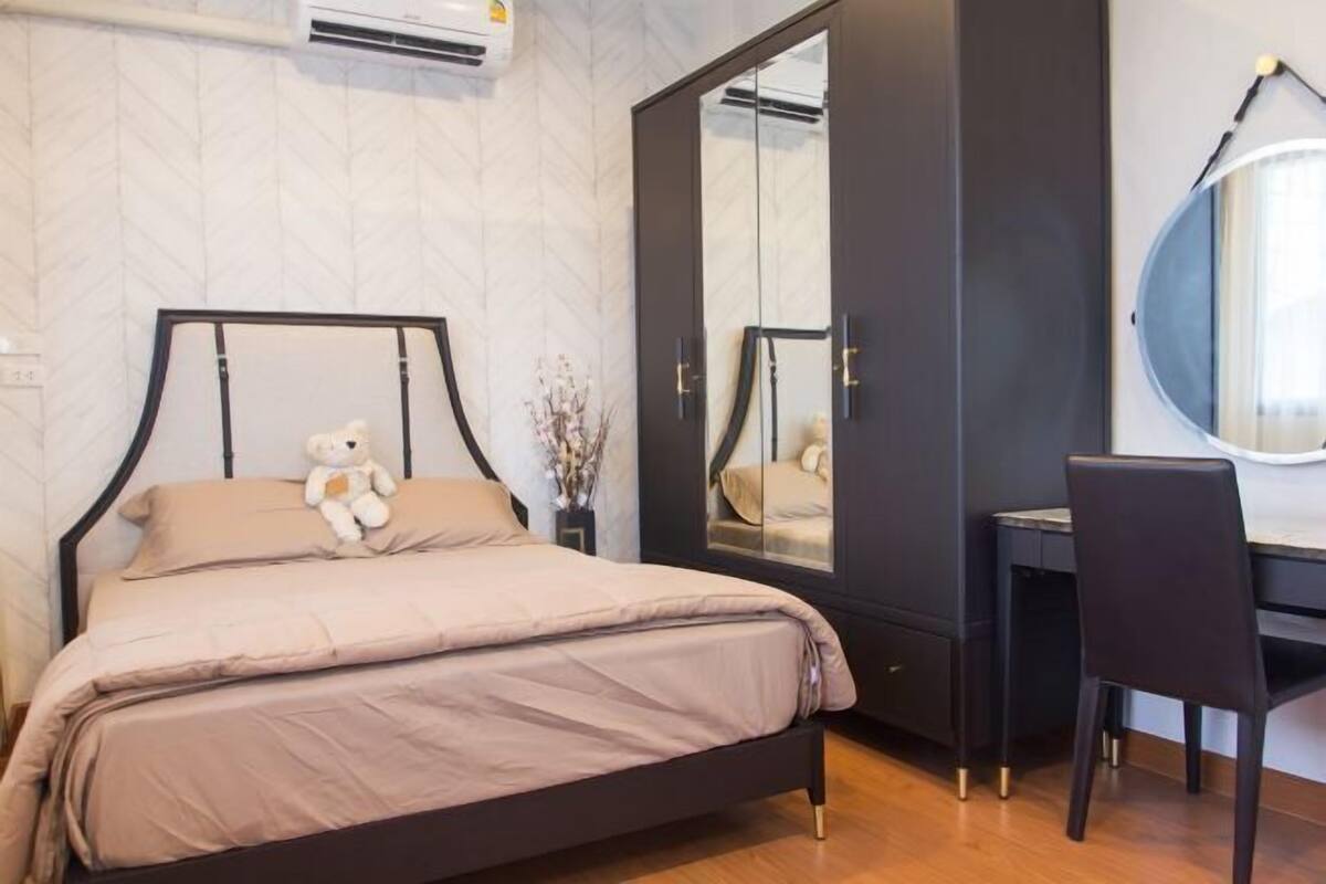 A bedroom with a bed, a desk, a chair, a wardrobe, and a mirror.