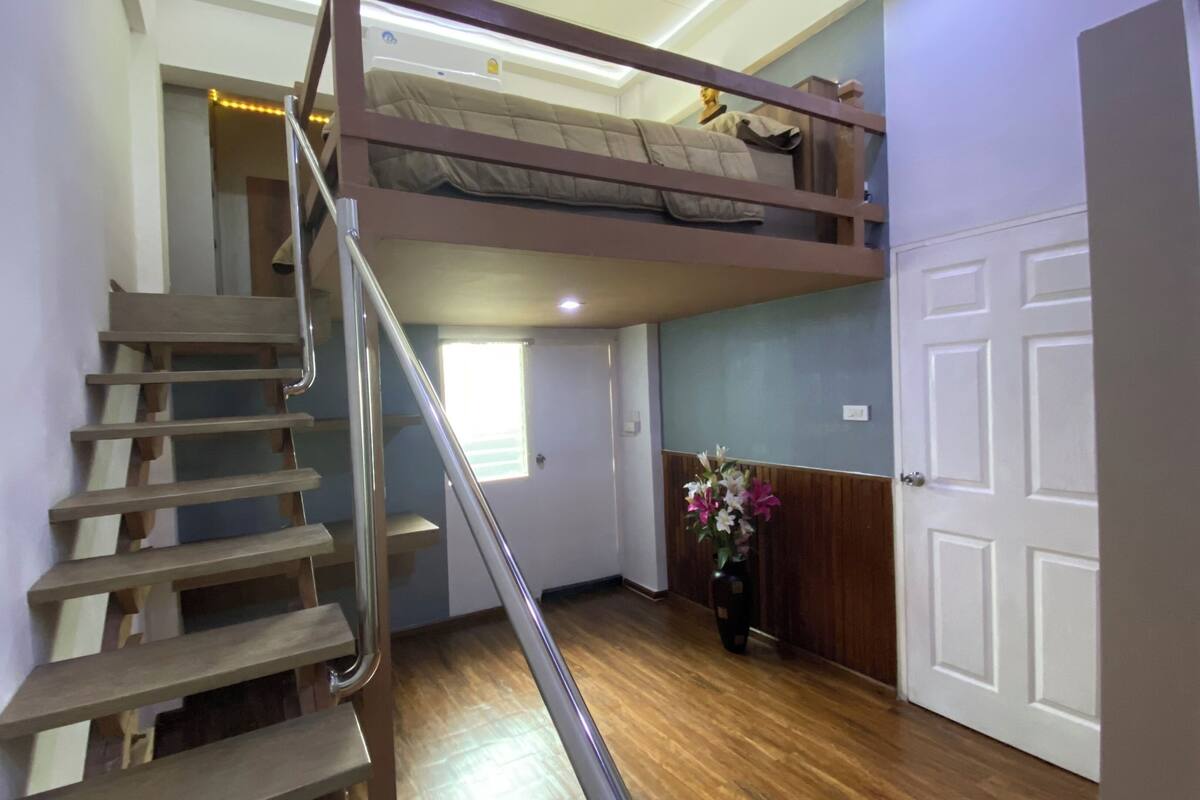 A room with a wooden staircase, a bunk bed, a door, and a vase with flowers.