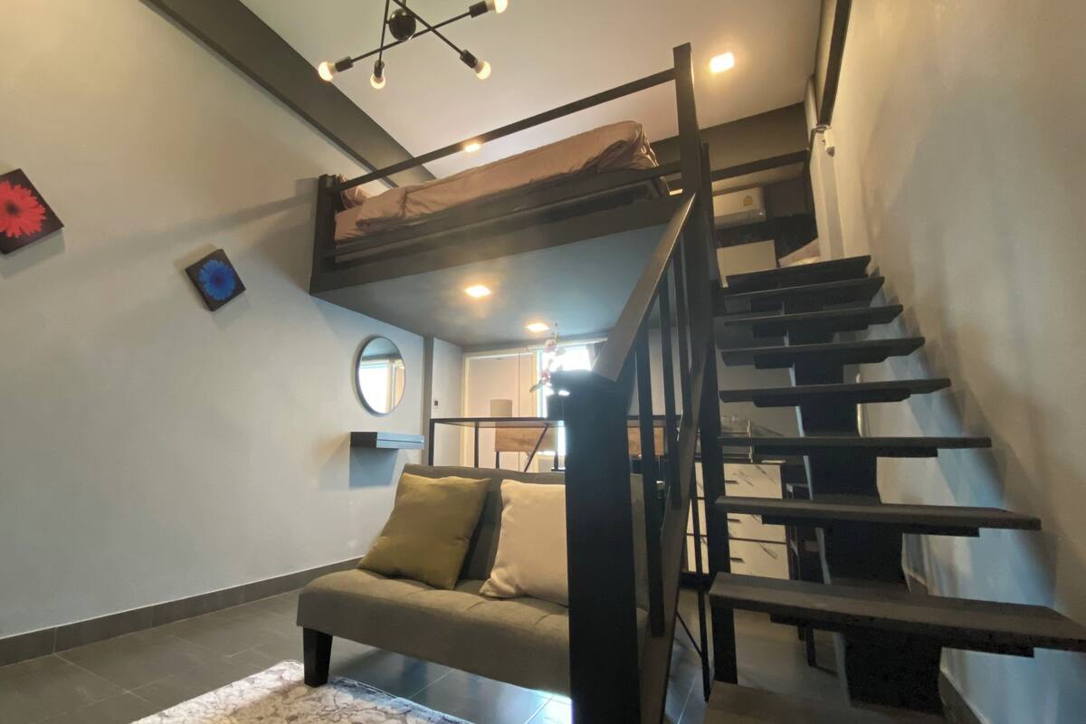 A modern interior with a bunk bed, a sofa, a mirror, and a staircase.