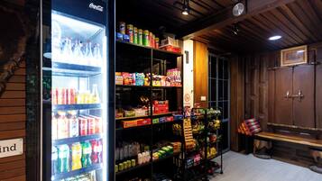 A room with a refrigerator stocked with beverages, shelves with snacks and toiletries, and a bench with a cushion.