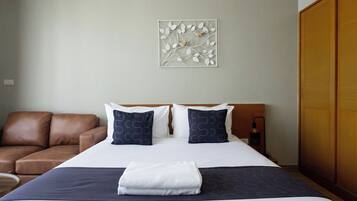 A hotel room with a bed, two pillows, a blanket, a brown leather sofa, and a wall-mounted artwork.