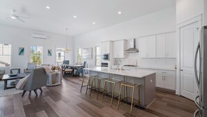 A modern kitchen with white cabinetry, a central island with stools, and a dining area with a sofa and chairs. - 🦩Book Me Baby! Pray For Sun~Private Home at Inlet Beach🦩 (Inlet Beach)