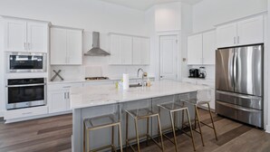 A modern kitchen with white cabinets, stainless steel appliances, and a marble island with bar stools. - 🦩Book Me Baby! Pray For Sun~Private Home at Inlet Beach🦩 (Inlet Beach)