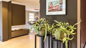 Een modern interieur met een donkere muur, een lijst met een foto en twee planten in potten op een zwart voetstuk.