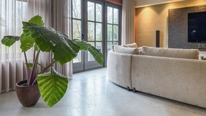 Een moderne woonkamer met een grote plant, een beige bank en een stenen open haard.