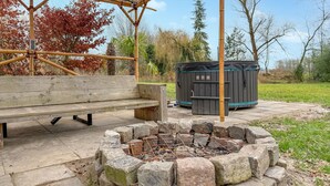 Een houten bank, een vuurkorf van steen en een jacuzzi in een tuin.