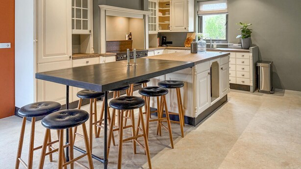 Een moderne keuken met een centraal eiland, barkrukken en witte kasten.