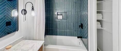 A modern bathroom with a bathtub, a vanity with a marble countertop, and a shower area with blue tiles.
