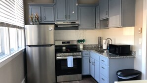 Una cocina compacta con armarios grises, electrodomésticos de acero inoxidable, un microondas y un lavabo.