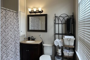A bathroom with a patterned shower curtain, a sink with a mirror above it, a toilet, and a towel rack with folded towels.
