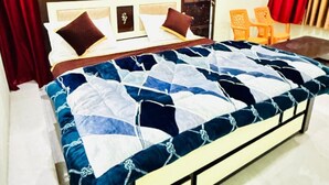 A hotel room with a bed, red and gold curtains, a wooden headboard, and a small table with chairs. - Goroomgo Shivaay Ayodhya (Faizabad)