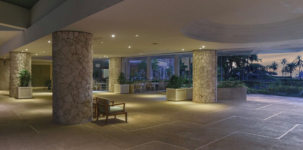 Un vestíbulo espacioso con columnas de piedra, zonas de estar y grandes ventanales con vistas al exterior.