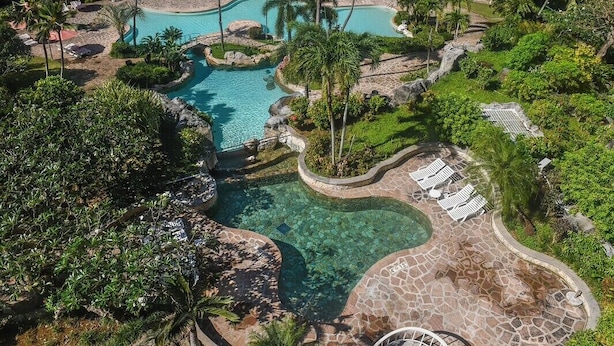 Un resort con varias piscinas, palmeras y vista al océano.