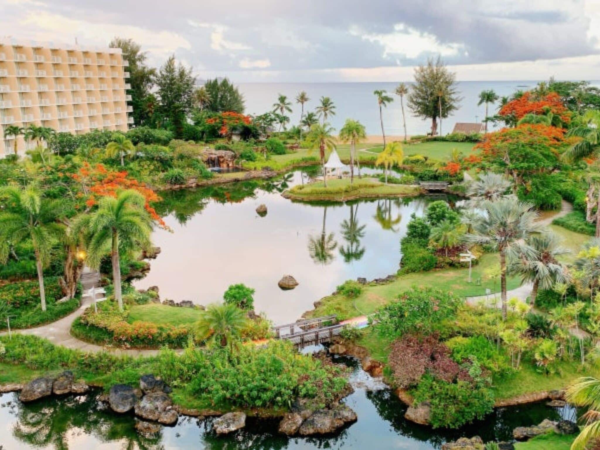 A resort with a large building, a pond, and tropical vegetation.