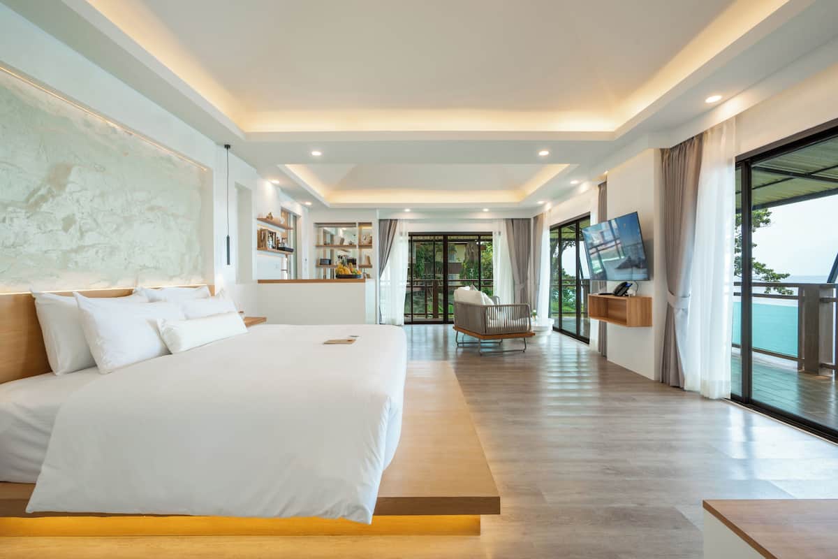 A modern hotel room with a large bed, a TV mounted on the wall, and a balcony with a view.