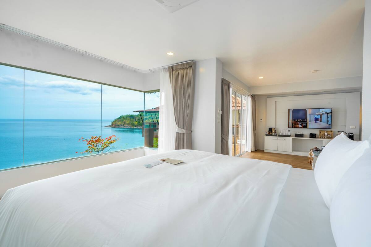 A hotel room with a large bed, a TV, and a view of the ocean.