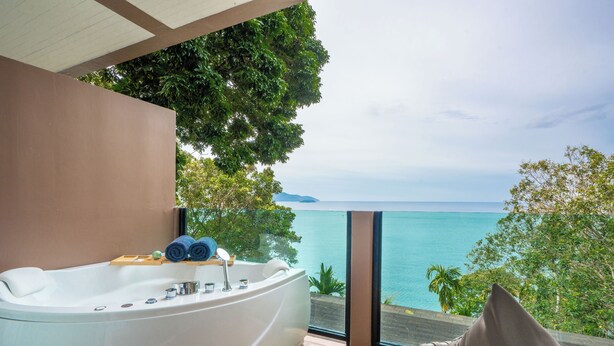 A modern bathroom with a large bathtub, a wooden side table, and a view of the ocean. - Anona Sunset Boutique (Karon)