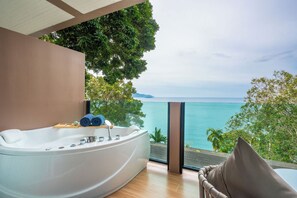 A modern bathroom with a large bathtub, a wooden side table, and a view of the ocean. - Anona Sunset Boutique (Karon)