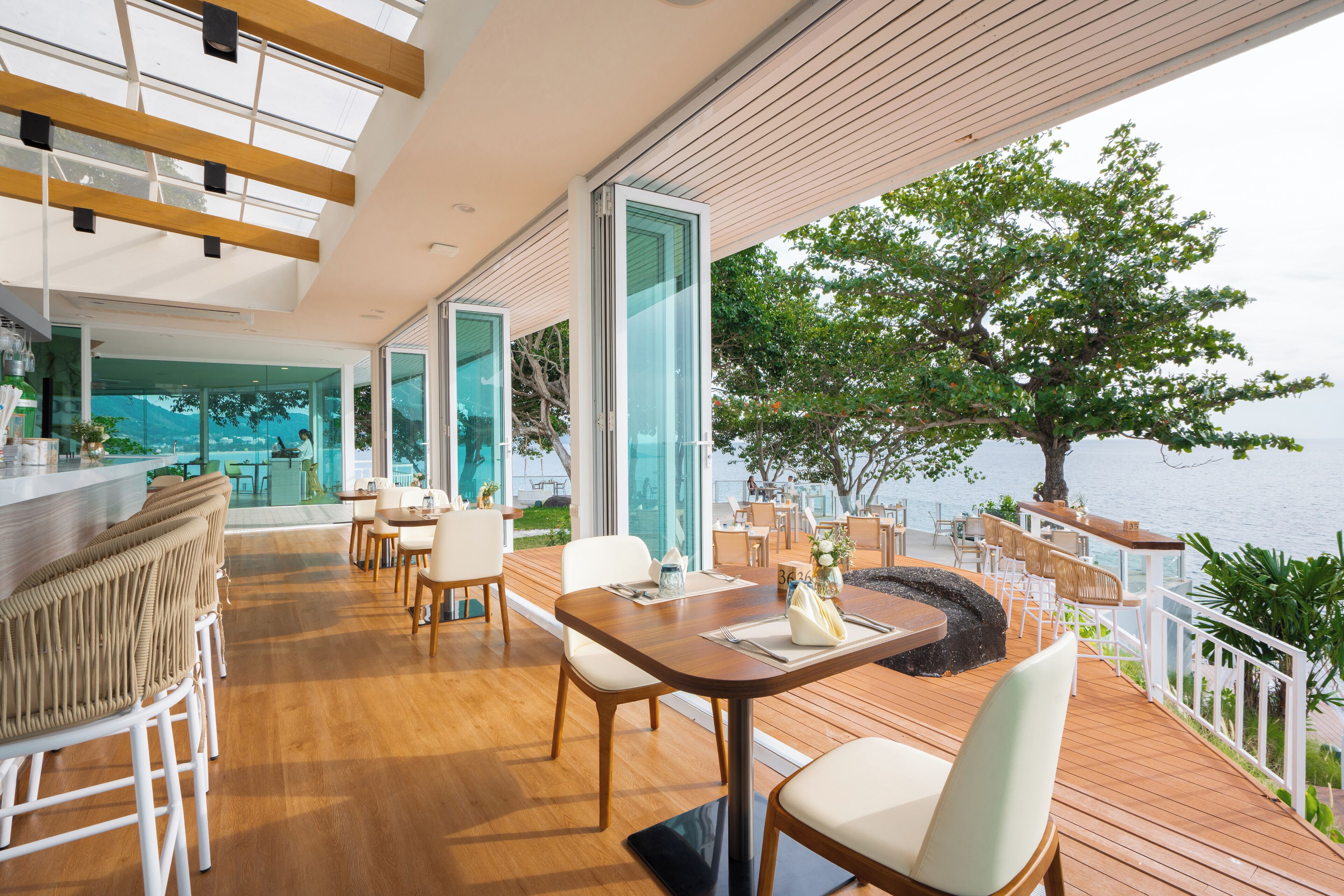 A modern outdoor dining area with wooden flooring, white chairs, and a central table.