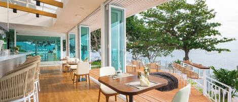 A modern outdoor dining area with wooden flooring, white chairs, and a central table.