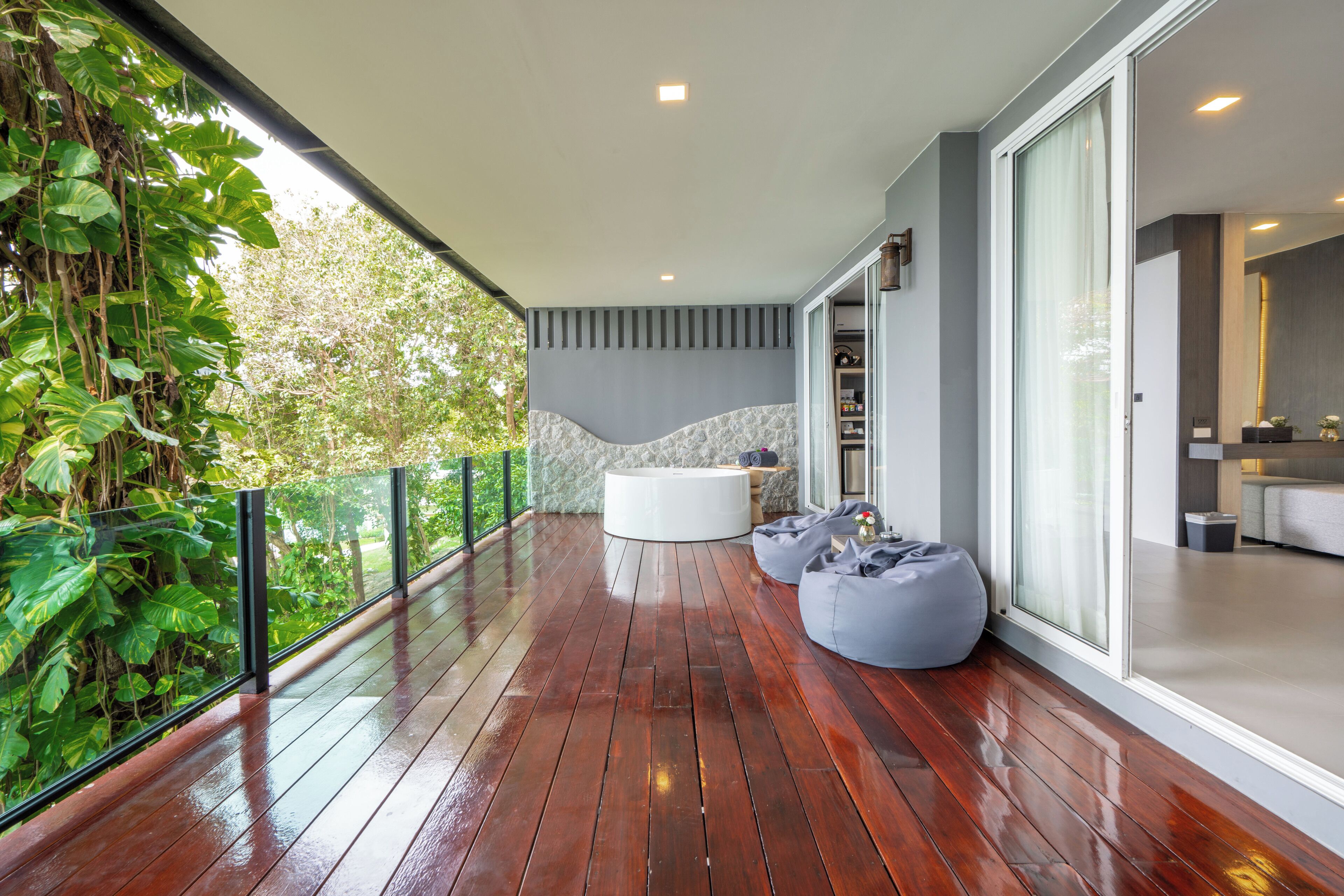 A modern balcony with a wooden floor, a white bathtub, and a grey bean bag.