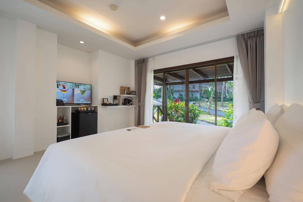 A hotel room with a large bed, a TV on a shelf, and a view of the outdoors.