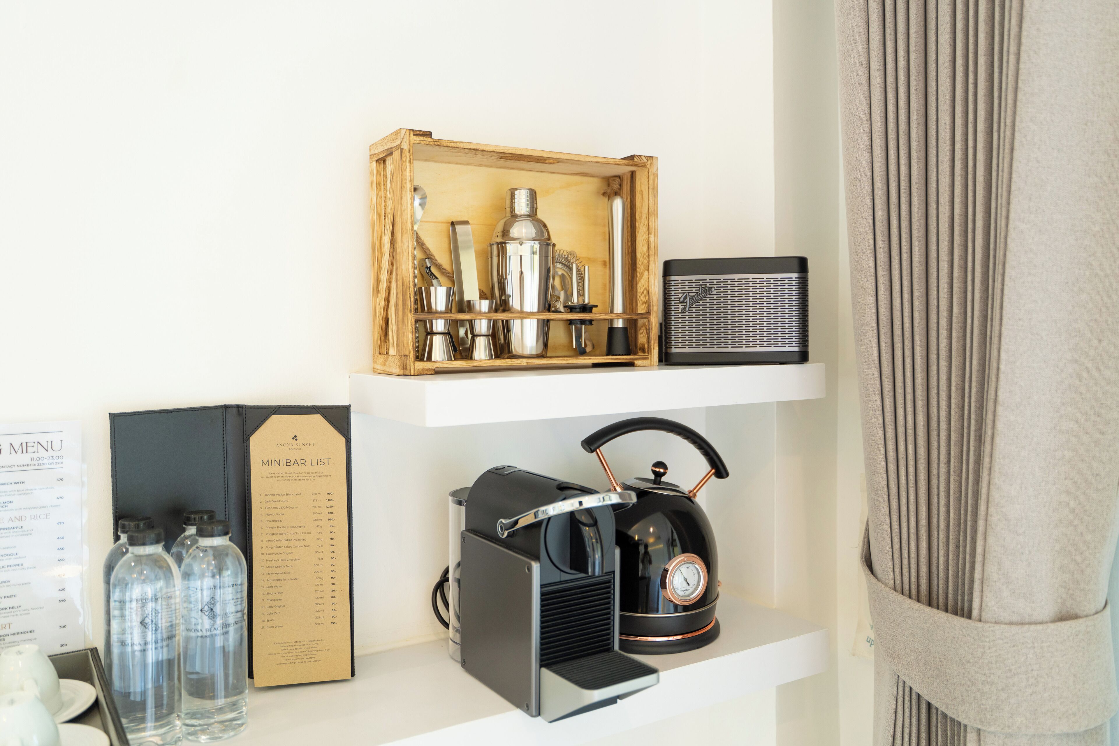 A minibar with a wooden box containing bottles and a radio, a kettle, and a menu on a white shelf.