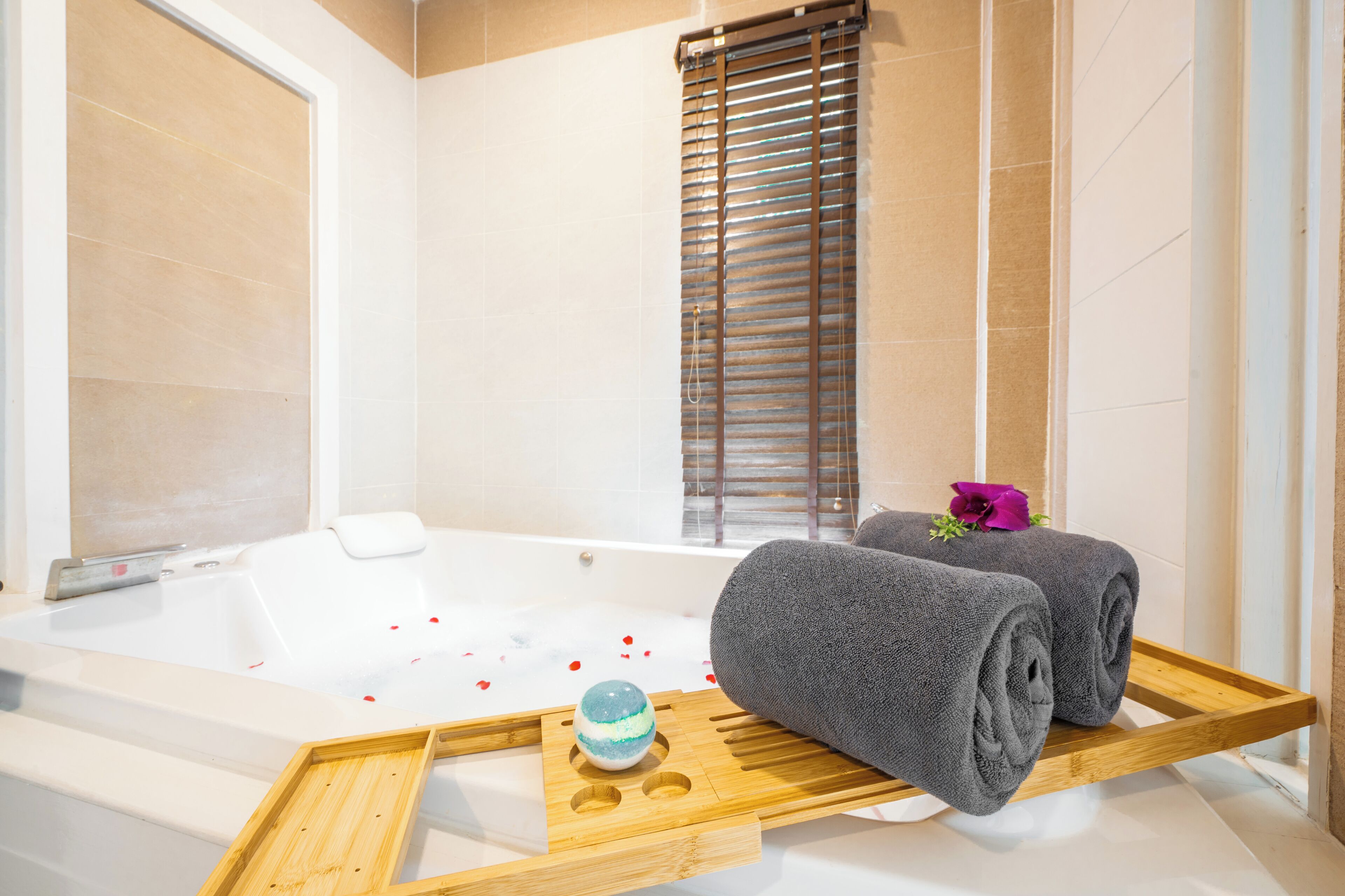 A modern bathroom with a bathtub, wooden tray, and towels.