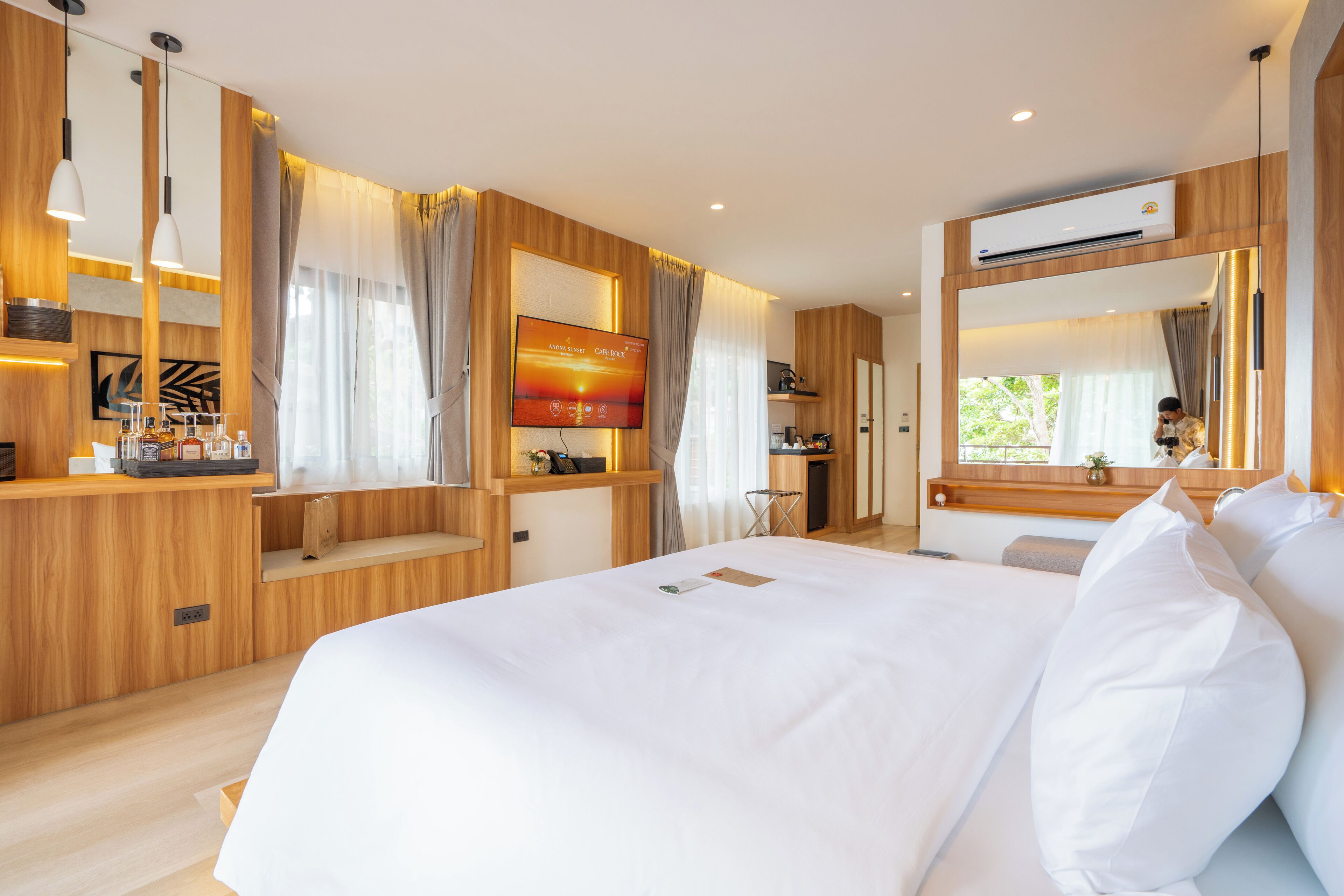 A modern hotel room with a large bed, a TV mounted on the wall, and a built-in desk with a mirror.
