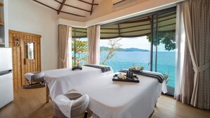 A room with two massage tables, a wooden door, and a view of the sea. - Anona Sunset Boutique (Karon)
