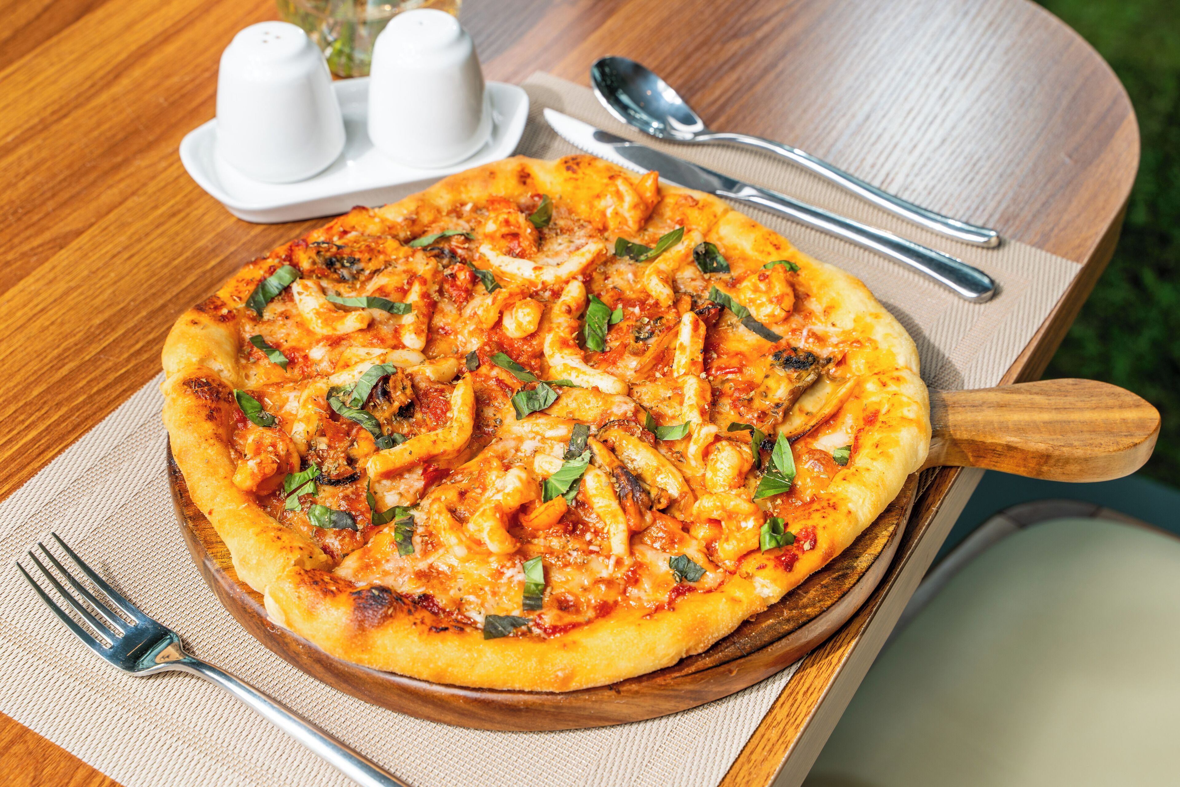 A pizza on a wooden board with a fork and knife beside it.