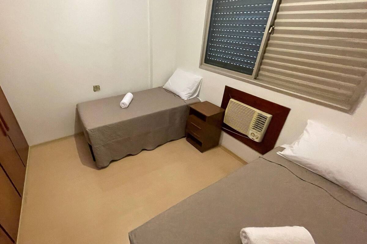 Una habitación pequeña con una cama individual, un armario de madera, una mesita de noche, un calentador y una ventana con persianas.