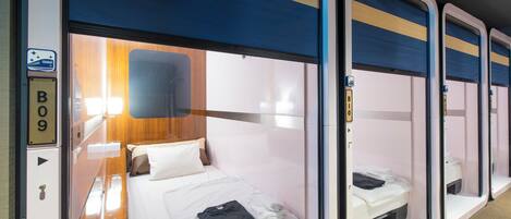 A train compartment with a single bed, a small table, and a wall-mounted shelf.