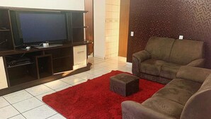 A living room with a flat-screen TV, a grey sofa, a red rug, and a tiled floor. - Regina Houses Sua Casa na Terra das Cataratas (Foz do Iguaçu)
