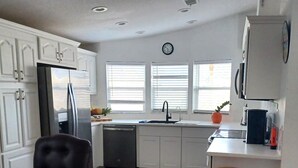 A modern kitchen with white cabinetry, a stainless steel refrigerator, a dishwasher, and a window with blinds. - Find your perfect home in Fort Myers - Affordable, comfortable & ready for you  (Fort Myers)