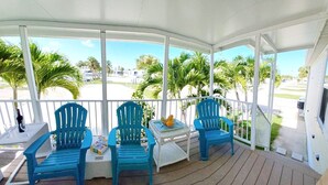 A covered porch with three blue chairs, a small table with a book and a bottle, and a view of palm trees and a road. - Find your perfect home in Fort Myers - Affordable, comfortable & ready for you  (Fort Myers)