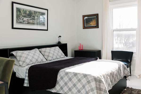 A bedroom with a bed, a nightstand, a chair, and two framed pictures on the wall.